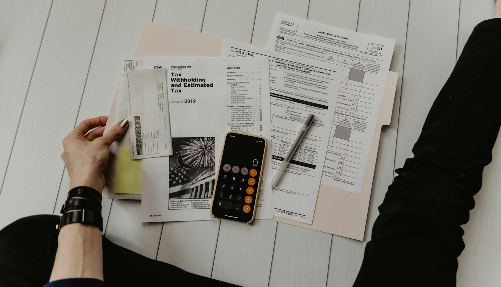 Person holding paper near a phone calculator and pen at a desk