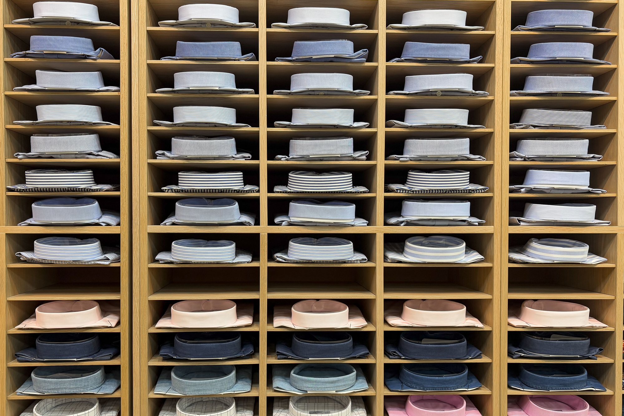 Dress shirts sorted by color and pattern in rows of wooden store cubbies
