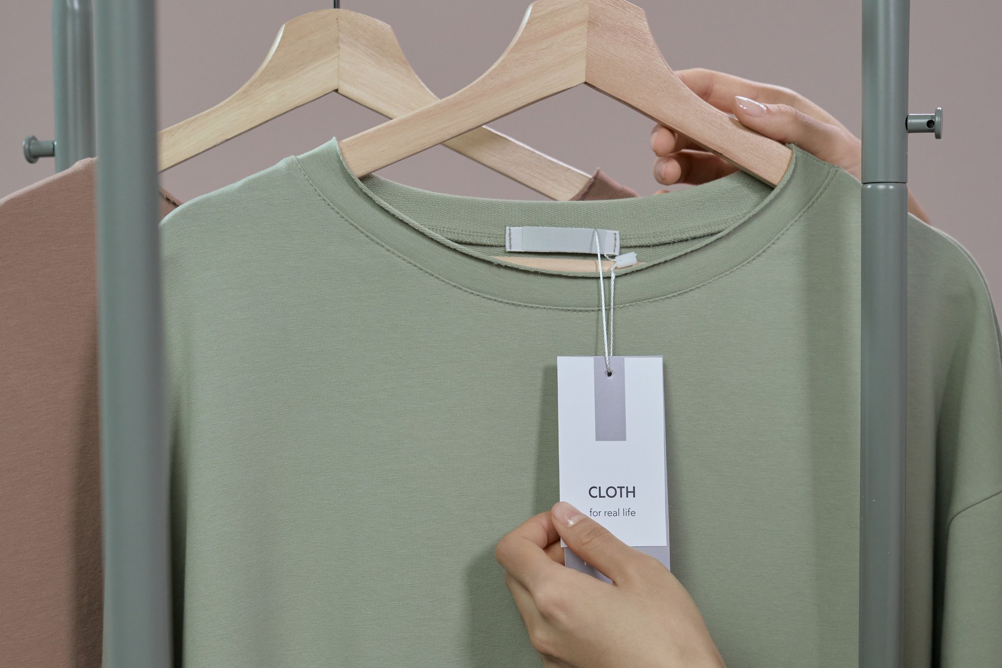A hand holds the hang tag of a sage green shirt on a wooden hanger